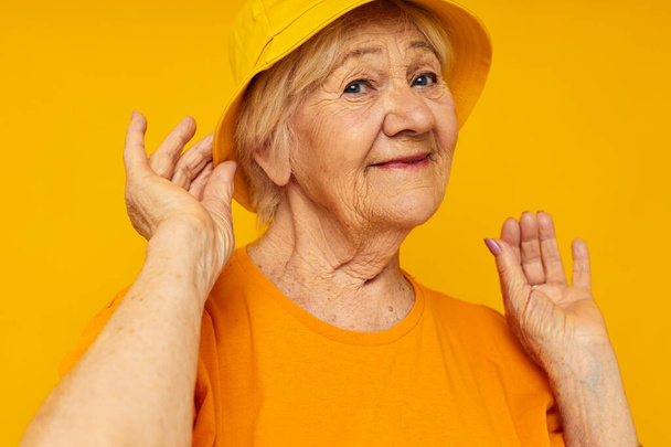 Portrait of an old friendly woman in yellow t-shirts hat posing cropped view - Photo, image