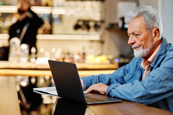Egy végzős diák ül az ebédlőben, és figyelemmel követi az online előadásokat a laptopján.. - Fotó, kép
