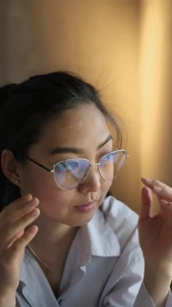 A thoughtful Asian woman takes off her glasses and puts them on the table. - Metraje, vídeo