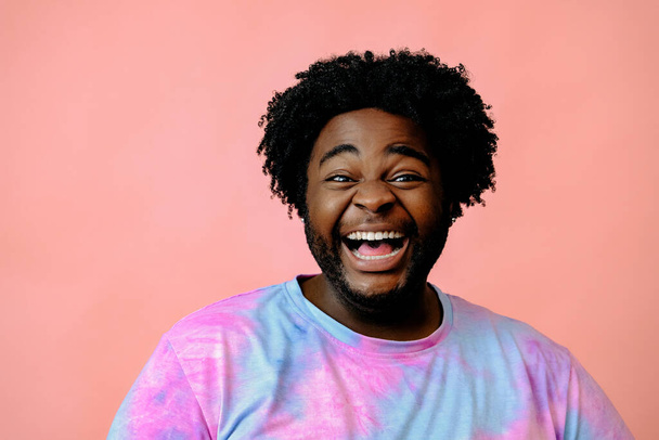 młody szczęśliwy Afroamerykanin człowiek pozowanie w studio na różowym tle  - Zdjęcie, obraz
