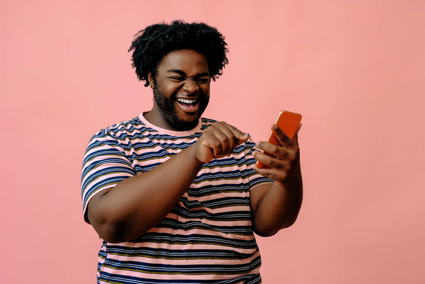mladý africký Američan s telefonem pózuje ve studiu přes růžové pozadí  - Fotografie, Obrázek