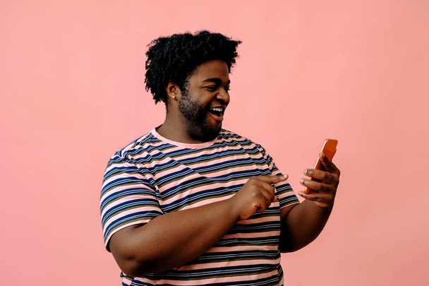young african american man with a phone posing in the studio over pink background  - Фото, изображение