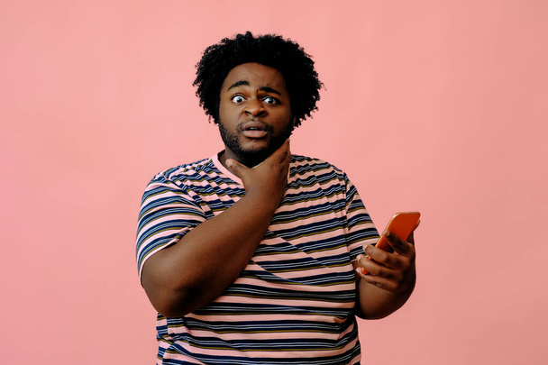 молодий афроамериканський чоловік з телефоном позує в студії на рожевому фоні
  - Фото, зображення