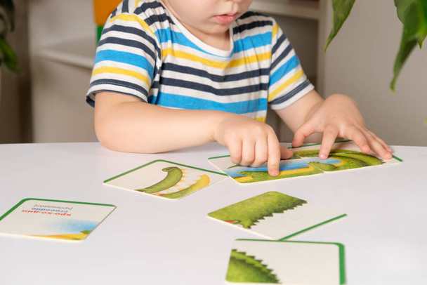Preschooler puts together a picture of a crocodile from puzzles, hands close-up. - Photo, image