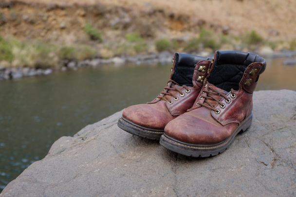 Old hiking boots beside river - 写真・画像