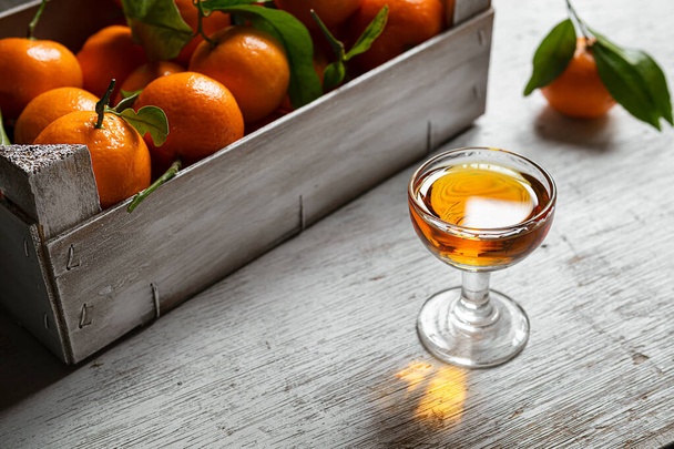 Tangerine liqueur shot and a box with fresh tangerines on on a white wooden table - Photo, image