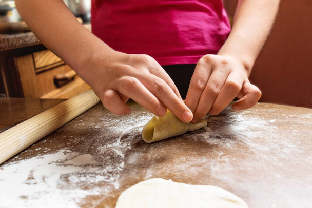 A child sculpts ravioli or dumplings from raw dough close-up. Selective focus. home kitchen in the kitchen - Fotó, kép
