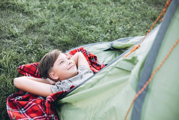 Nastolatek leżący na kratę w namiocie kempingowym. Rodzinny weekend na świeżym powietrzu. - Zdjęcie, obraz