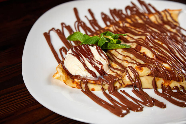 Pancake with a scoop of ice cream and chocolate. Close-up, selective focus - 写真・画像