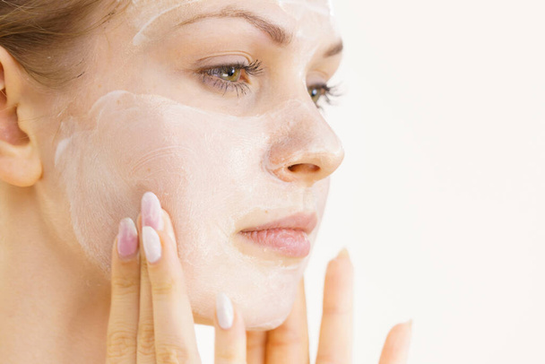 Young woman applying cream cosmetic, mask moisturizing to her face. Beauty treatment. Skincare. - Fotó, kép