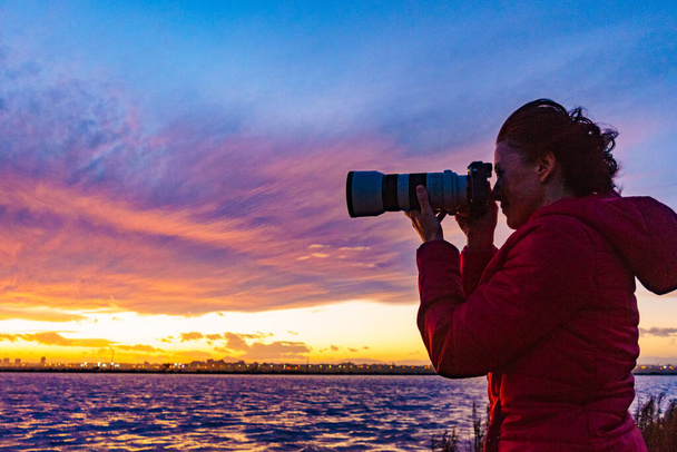 Woman photographing seascape at sunset with professional camera. - 写真・画像