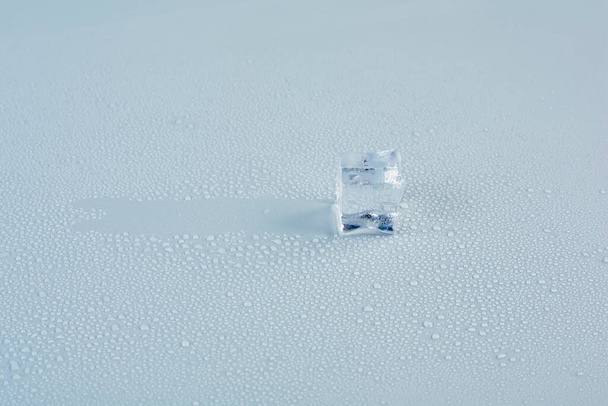 An ice cube glides across a gray background in drops of meltwater - Foto, Bild