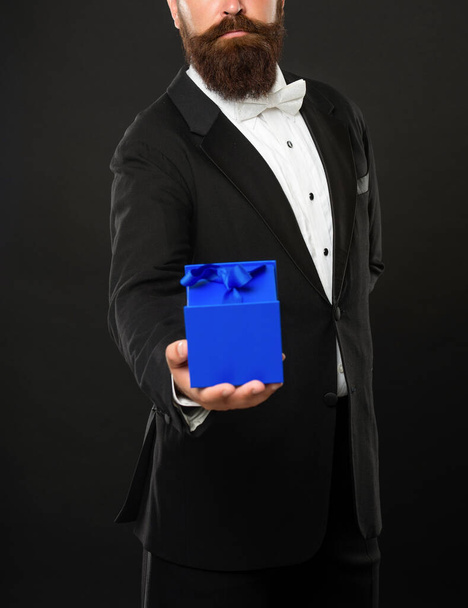 cropped gentleman in tuxedo bow tie formalwear on black background with gift box. boxing day - Foto, Bild