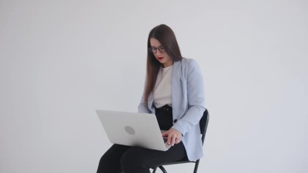 Fuerte confianza de negocios de la risa en gafas negras sentado con el ordenador portátil en su regazo en blanco aislado de fondo y el uso de touchpad - Metraje, vídeo