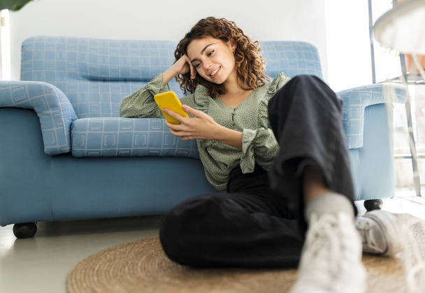 curly haired woman sitting on sofa with mobile phone - Fotoğraf, Görsel