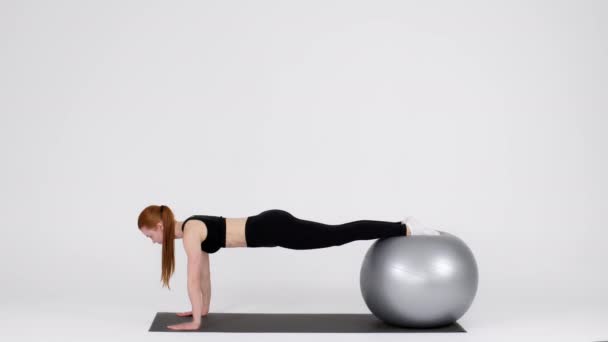 Joven mujer deportiva haciendo ejercicio de tablón mientras se equilibra en Fitball en el estudio - Metraje, vídeo