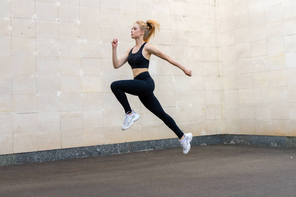 Sport and Fitness Concept Young Adult Caucasian Female Athlete Jumping High Outdoor Gray Tail Wall Background Sportive Woman Jump Exercises Outside Healthy Lifestyle Motivation - Foto, immagini