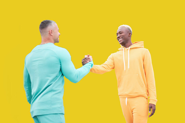 Multi ethnic friends. Two men different color black African-American ethnicity and white Caucasian ethnicity standing isolated yellow background. Handshake. interracial friendship - Photo, image