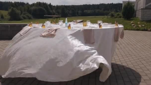 Beautifully decorated table for a celebration with a tablecloth fluttering in the wind and small jars of honey for guests on an open area - Filmagem, Vídeo