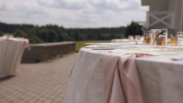 Tables on the terrace with glassware and honey jars for guests at a wedding party in nature. The camera changes focus - Materiał filmowy, wideo