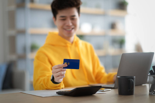 Χαμογελαστή ασιατική τύπος δείχνει χρησιμοποιώντας πιστωτική κάρτα στο σπίτι - Φωτογραφία, εικόνα