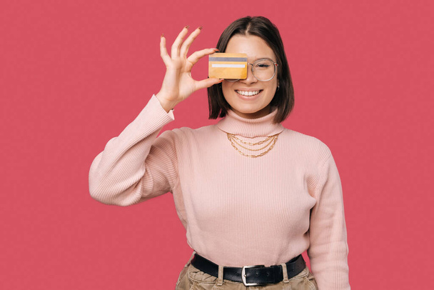 Foto de la alegre joven mujer de moda sosteniendo la tarjeta de crédito amarilla sobre los ojos y mirando a la cámara - Foto, imagen