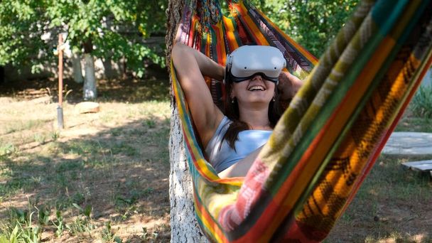 Nainen yllään virtuaalitodellisuus lasit lepää riippumatossa lähellä puuta, kuvitellen unelma toteutuu, keksitty maailma. Käsite saada kokemusta käyttämällä VR kuulokkeet lasit virtuaalitodellisuus - Valokuva, kuva
