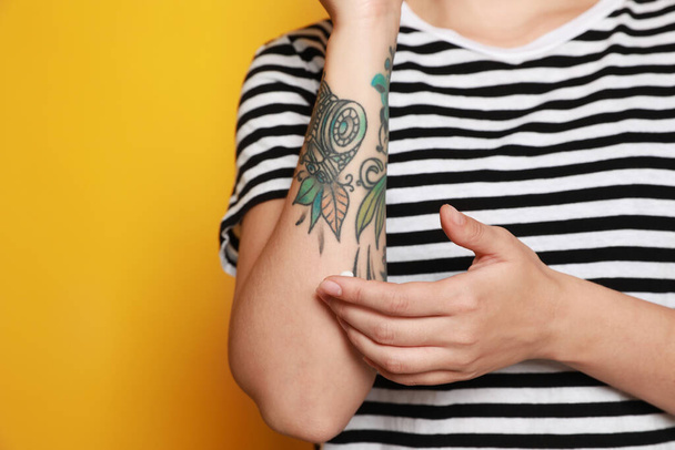 Woman applying cream on her arm with tattoos against yellow background, closeup. Space for text - Foto, Imagem