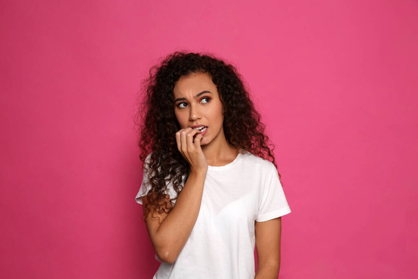 African-American woman biting her nails on pink background - Fotó, kép