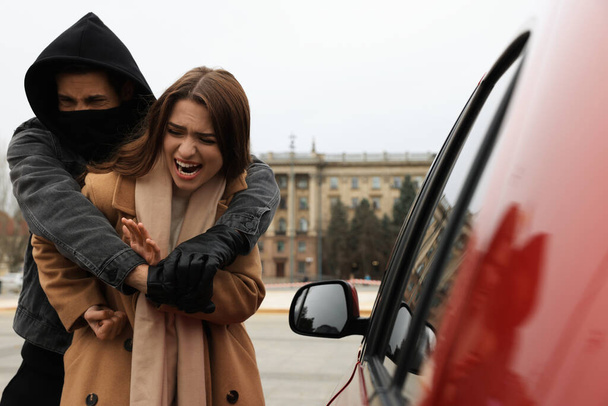 Woman defending herself from attacker near car outdoors - Fotografie, Obrázek