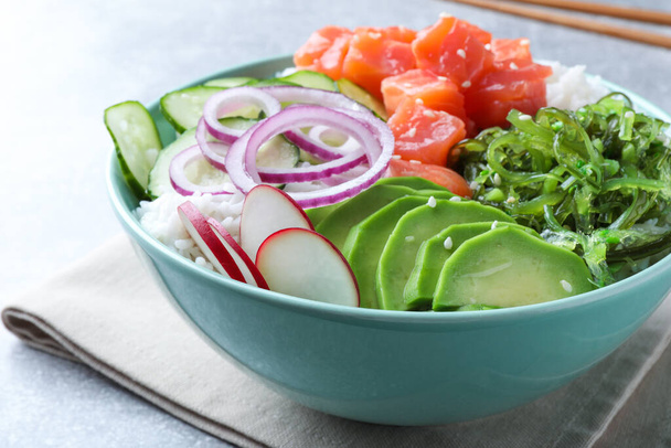 Delicious poke bowl with salmon, seaweed and vegetables served on light grey table, closeup - Zdjęcie, obraz