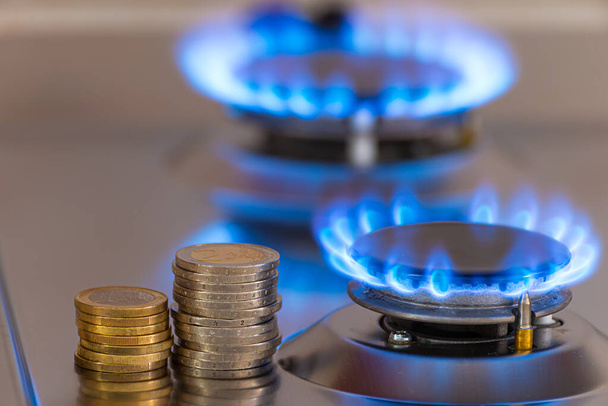 Gas stove lit, with stacks of coins above it. Increase in gas costs and tariffs. - Photo, Image
