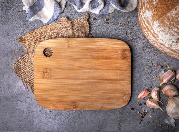 Kitchen composition with wood cutting board, spices, garlic, bread on dark stone countertop, background, blackboard. Horizontal banner with a copy-space, text space. Culinary concept, table top view. - Fotó, kép