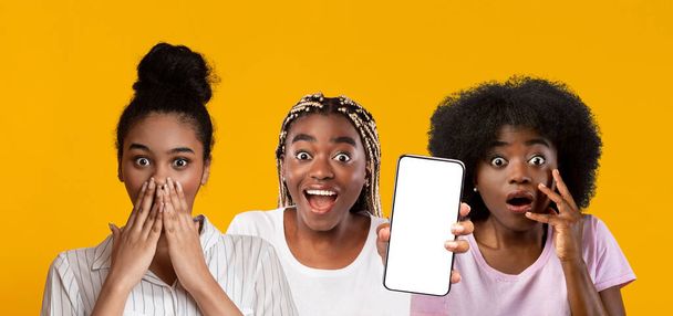 Amazed black women showing smartphone with empty screen, mockup - 写真・画像