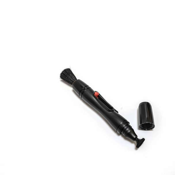 A device for cleaning camera lenses. A black plastic pencil with a retractable brush on one end and a soft cleaning disc on the other. The cap is nearby. Isolated on a white background - Foto, afbeelding