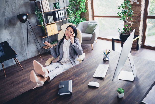 Full body photo of successful ceo lady sitting chair legs on desktop speak telephone wear grey jacket indoors. - Foto, Imagen