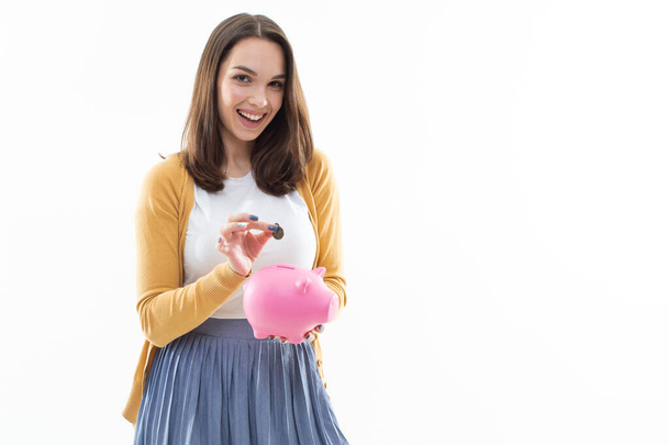 Girl collects money in a pink piggy bank on a white background - Foto, afbeelding