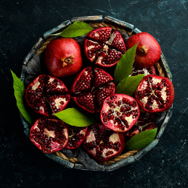 Healthy pomegranate fruit with leaves and open pomegranate in a wooden box. Top view. - Photo, image