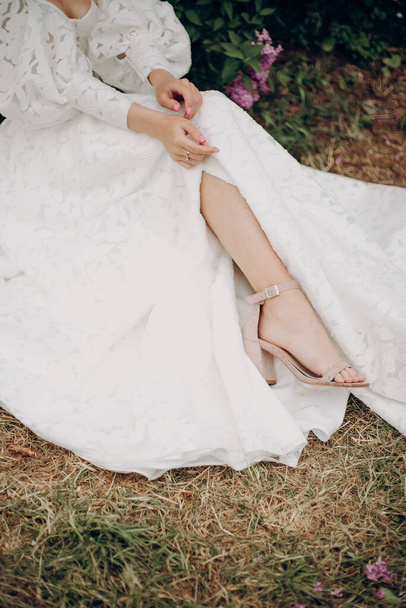 Молода блондинка в білій весільній сукні з відкритим верхом біля бузку
 - Фото, зображення