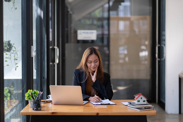 Бізнес азіатська жінка або агент з нерухомості, що працює з ноутбуком в її офісі
 - Фото, зображення