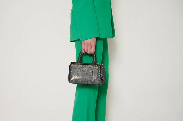 Girl in green suit with shiny black handbag in her hand. Green pants and blazer with fashionable accessory. Horizontal photo with copy space. - Foto, afbeelding