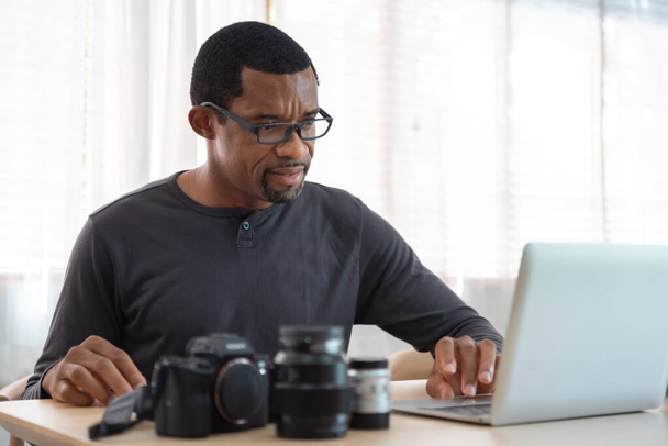 Serious African American photographer man using laptop computer, Black Freelancer working at home studio. - Φωτογραφία, εικόνα