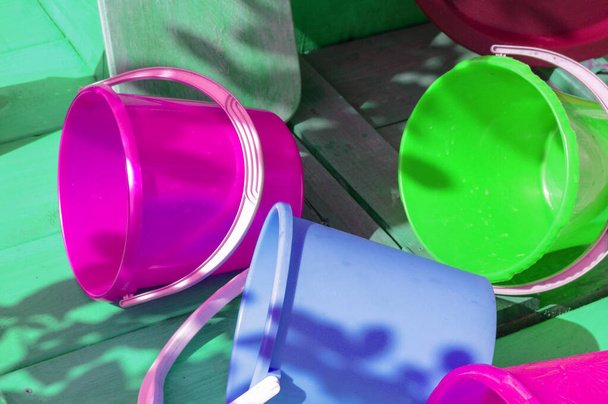 Разноцветная пустая чистая пластиковая посуда на деревянном фоне, на открытом воздухе, в солнечный летний день. - Фото, изображение