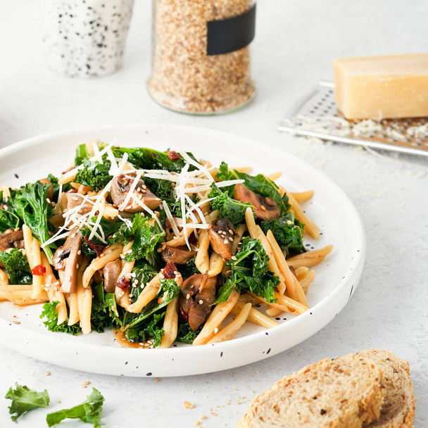 Whole grain pasta with kale, mushrooms, parmezan cheese in white plate on light background. Vegetarian Healthy diet concept. Recipe step by step. - Zdjęcie, obraz