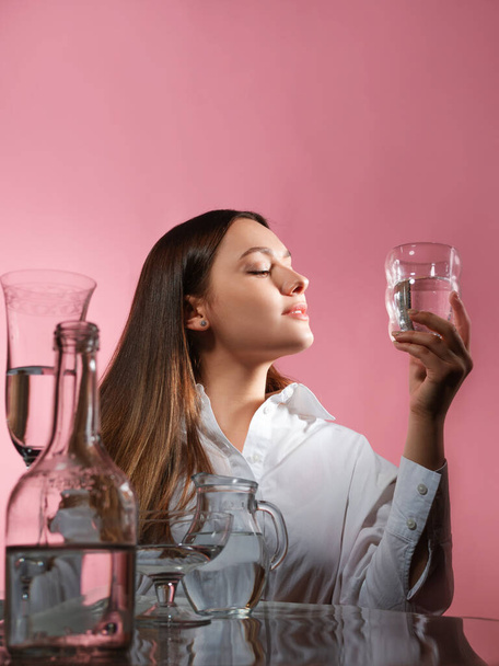 A beautiful young brunette holds a glass of clean water in her hands, - Фото, изображение