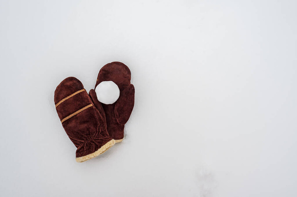 Snowball on brown suede warm mittens, in the snow. Winter active games and entertainment. Copy space.  - Фото, изображение