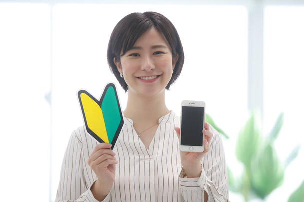 Female employee with smartphone and beginner mark  - 写真・画像