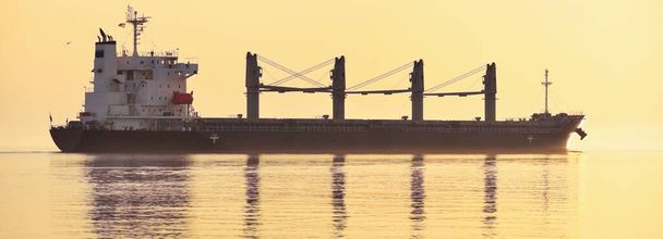 Grand cargo naviguant dans la mer Baltique au coucher du soleil. Doux soleil doré. Concept paysage marin. Vue panoramique depuis le voilier. Transport de marchandises, navire nautique, logistique - Photo, image