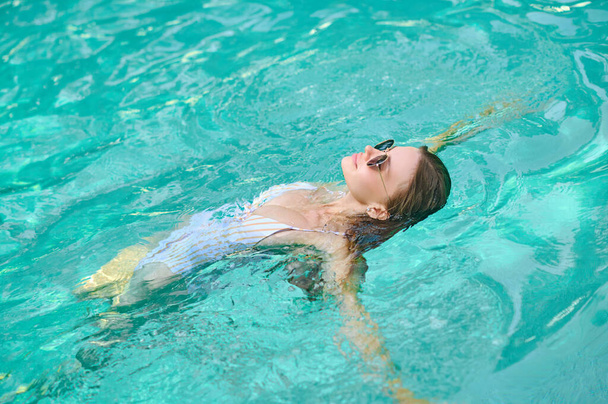Young woman laying on water and looking relaxed - Photo, image
