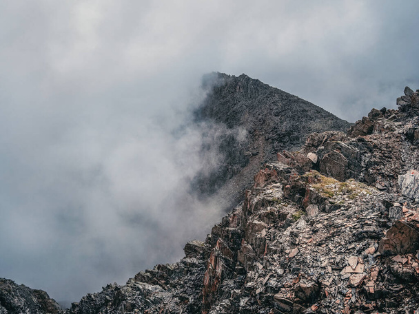 Θέα στο βουνό από γκρεμό σε μεγάλο υψόμετρο. Μυστικό τοπίο με όμορφα κοφτερά βράχια κοντά σε γκρεμό και λούκια σε χαμηλά σύννεφα. Όμορφο ορεινό ομιχλώδες τοπίο στην άκρη της αβύσσου με αιχμηρές πέτρες. - Φωτογραφία, εικόνα